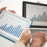 Um tablet e uma tela de computador mostrando gráficos representando lucro