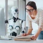 A humanoid robot sits beside a woman in a modern office, both focused on documents and a computer screen, illustrating human-AI collaboration in the workplace, representing AI agents