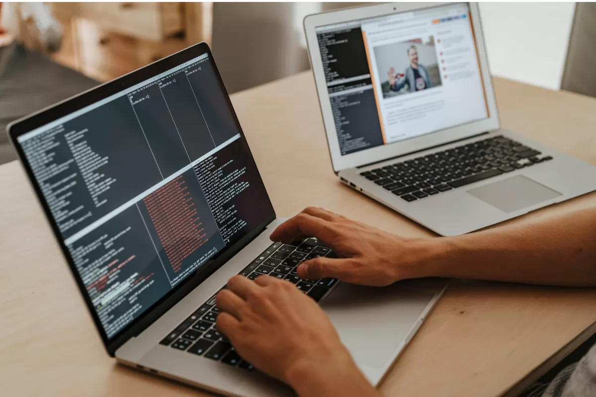 Person working on two laptops, running code and testing integrations between systems and APIs.