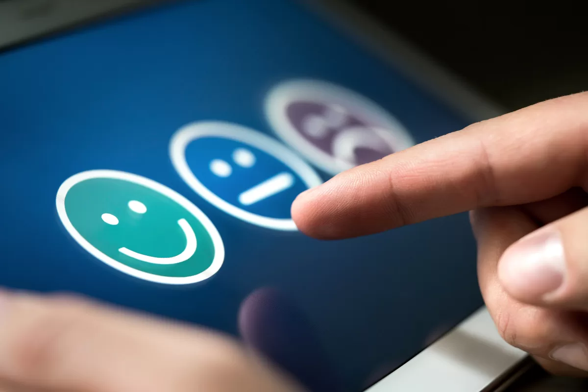 Person selecting a happy face icon on a touchscreen feedback survey, representing Performance Bottlenecks 