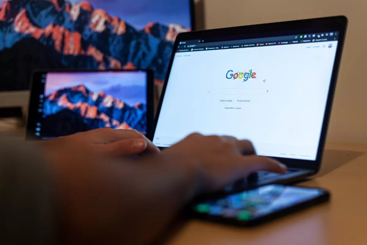 Person typing on a laptop with Google’s homepage open, with two additional screens visible in the background.