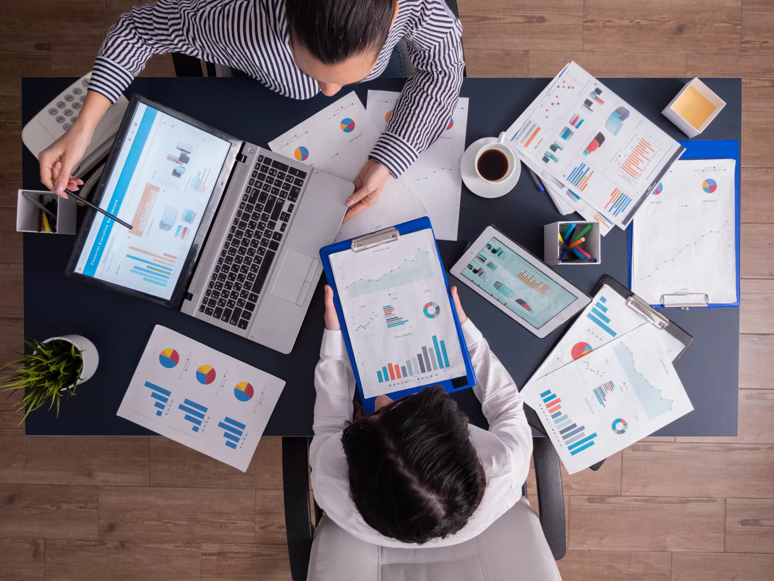 Top view of two people in a business meeting analyzing charts on laptops and tablets, symbolizing data-driven decision-making and productivity in companies. 