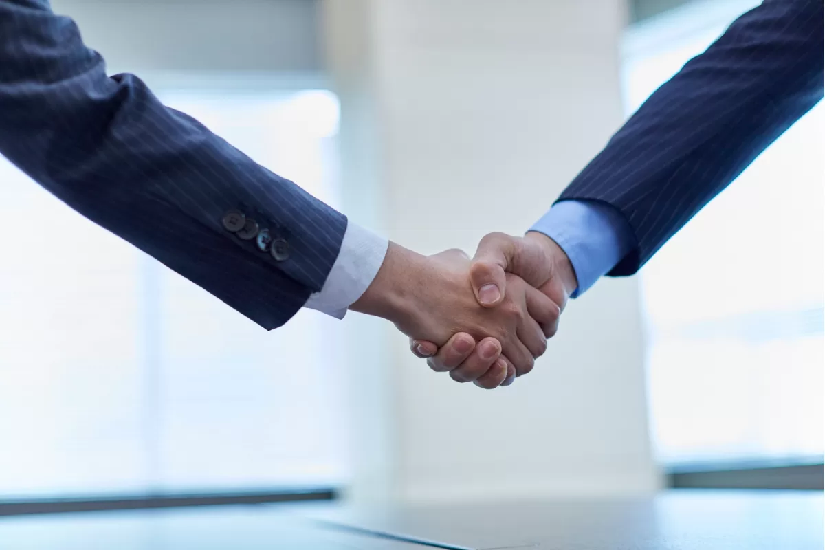 Close-up of two business professionals in suits shaking hands, representing agreement and alignment between teams