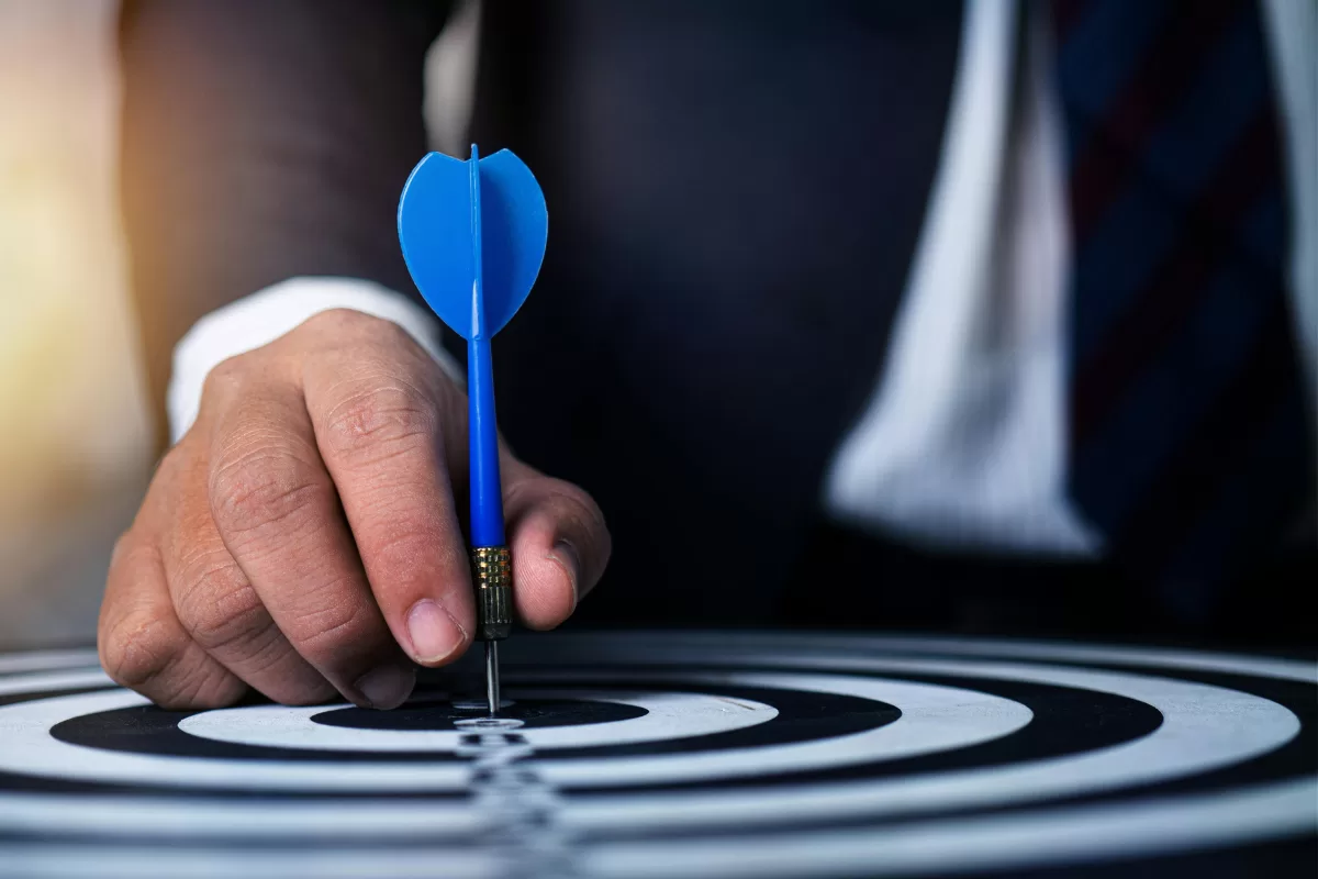 Businessperson holding a blue dart hitting the bullseye of a target, representing focus and goal achievement.