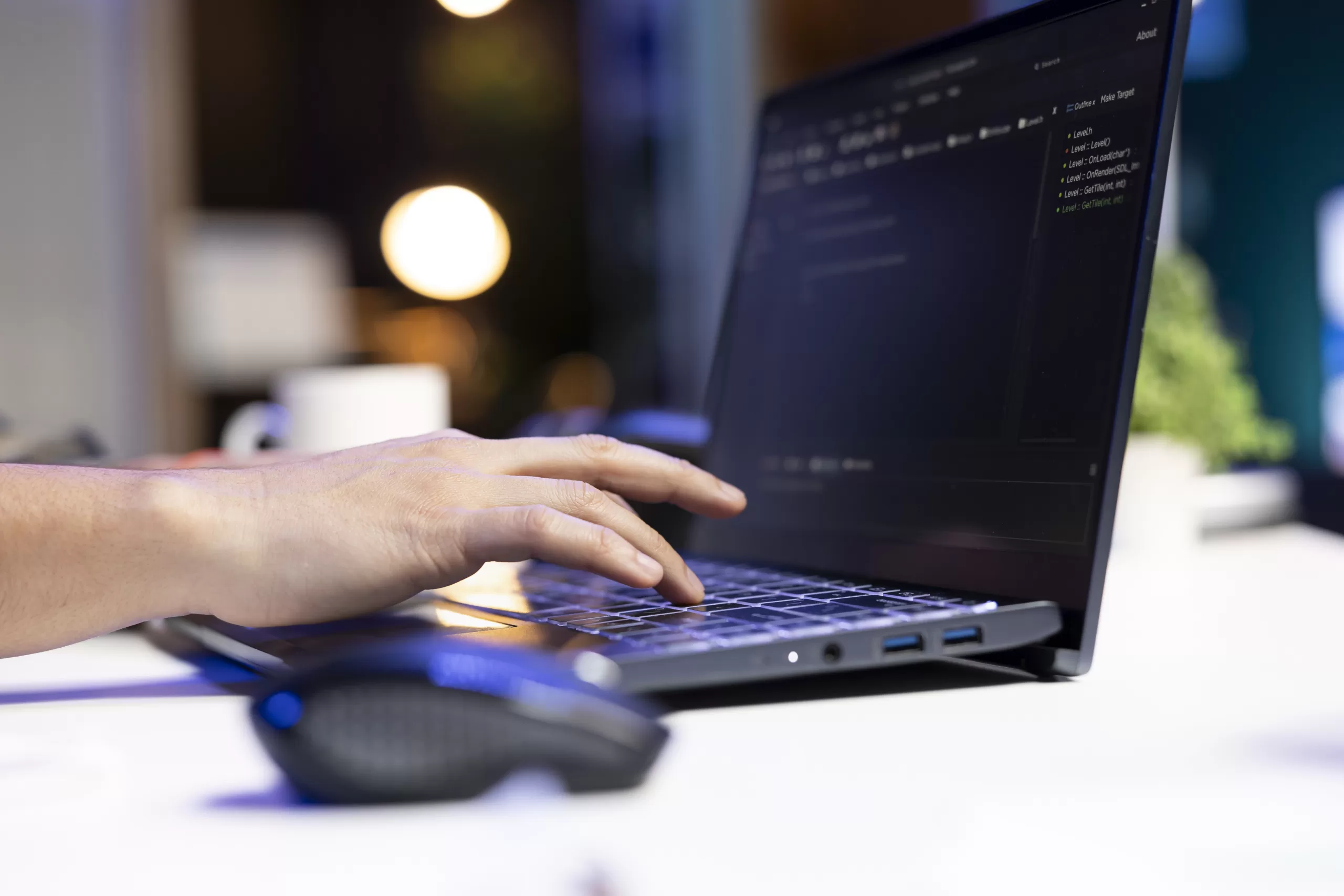 Close-up of a person’s hand typing on a laptop keyboard with code displayed on the screen.