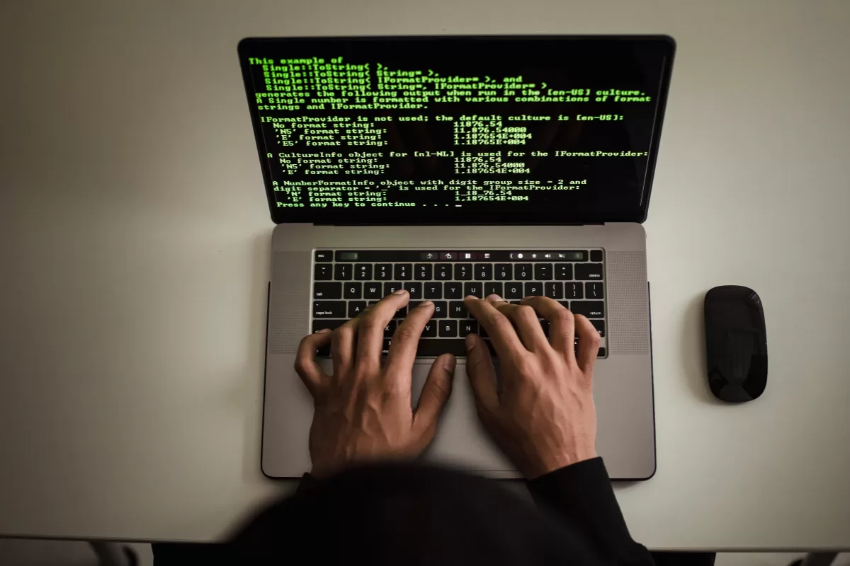 Person typing on a laptop showing green code on a black screen, symbolizing software development and technical work.