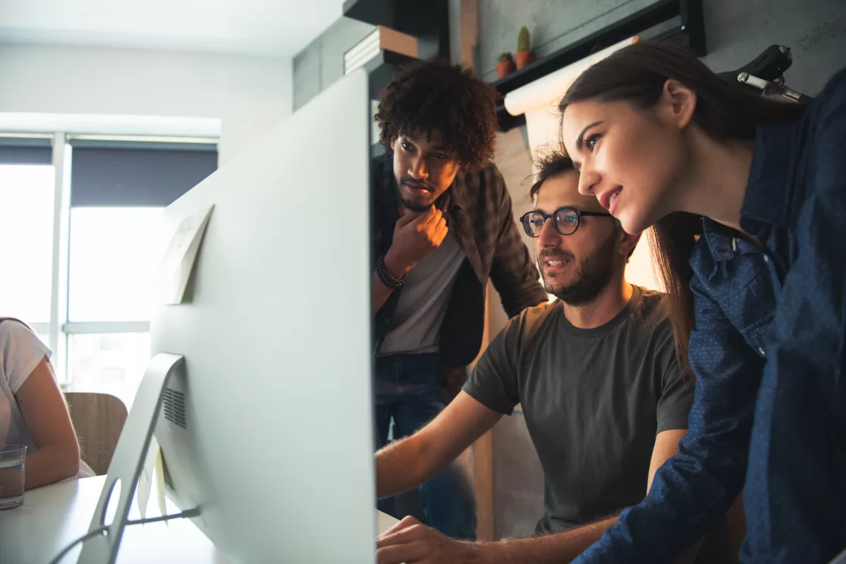 Three colleagues collaborating and closely watching a computer monitor.