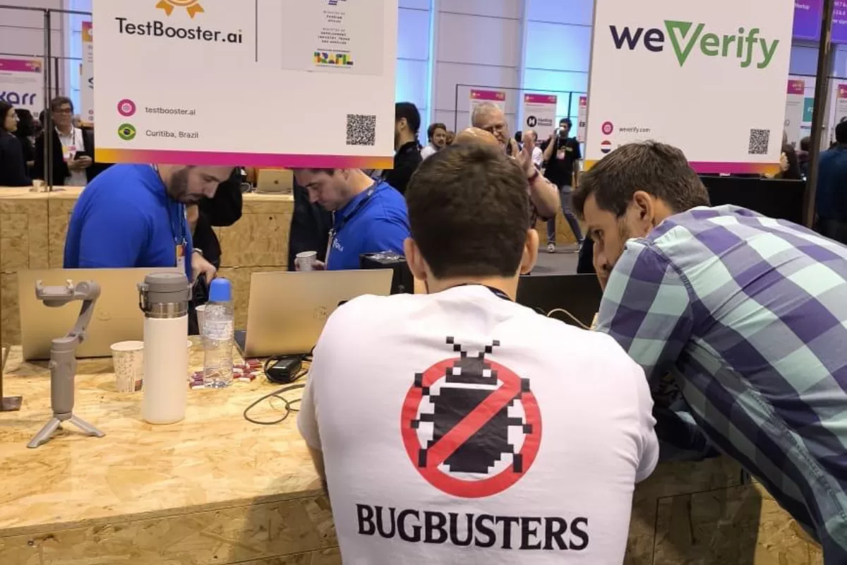 Estande do TestBooster.ai no Web Summit Lisboa 2025 com visitantes conversando, equipe usando camiseta Bugbusters e banner da plataforma de testes de software com IA ao fundo.