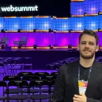 Gustavo Liu, COO do TestBooster.ai, no palco principal do Web Summit Lisboa 2025 com telão e iluminação roxa ao fundo