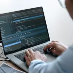 Programador digitando código em laptop com editor de desenvolvimento aberto mostrando linhas de código em tela escura, representando testes de API e E2E