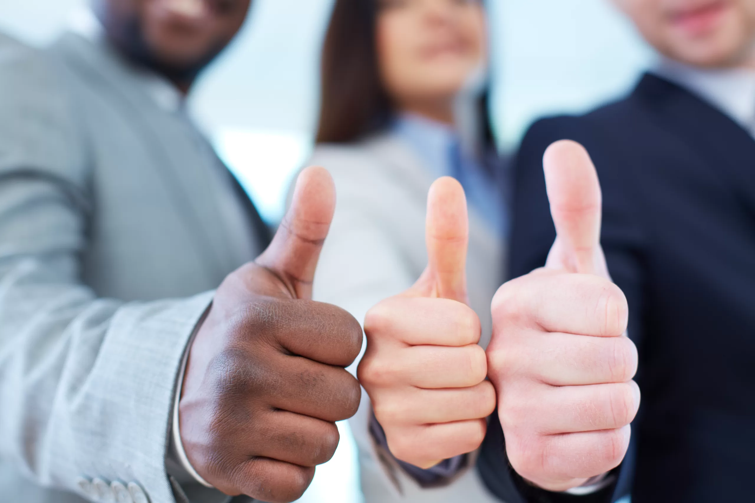 Three people in business attire giving a thumbs-up gesture with their hands in focus.