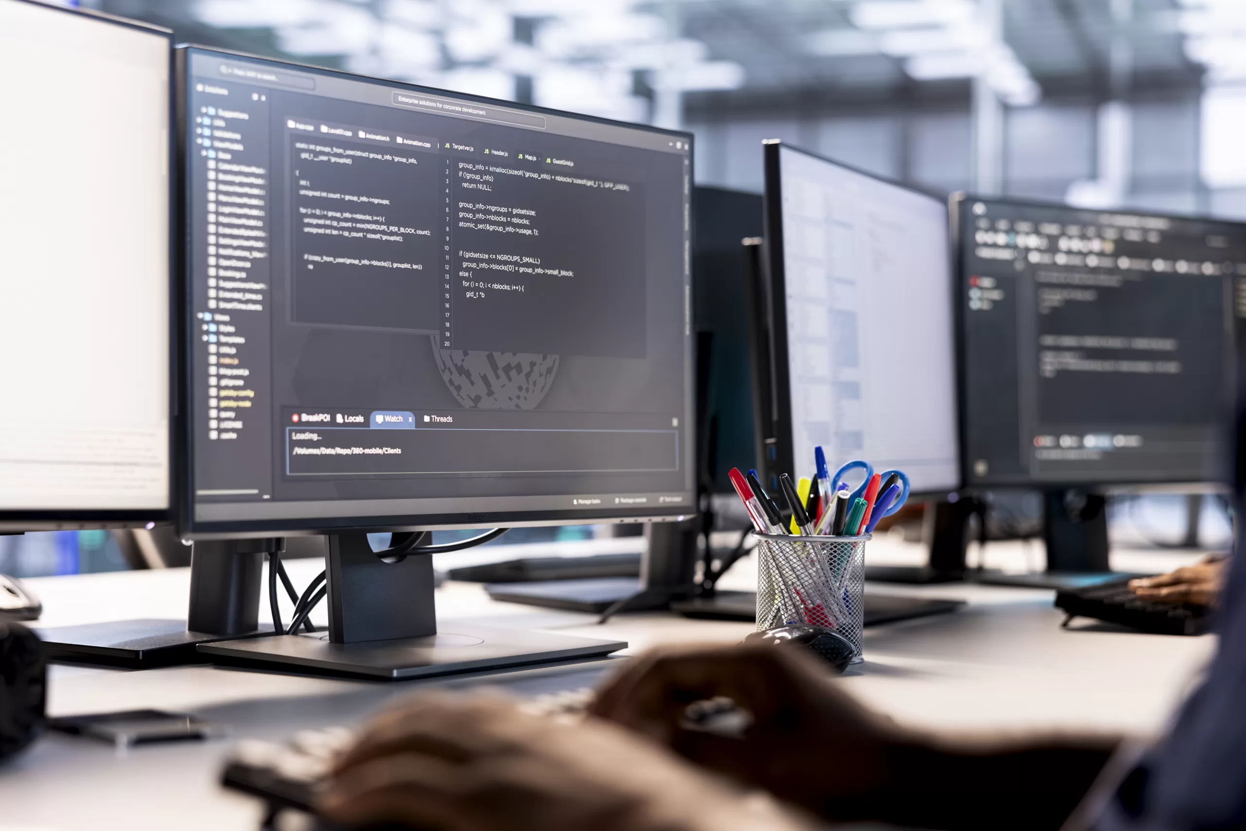 Person holding a tablet with programming code, with monitors showing code in the background.