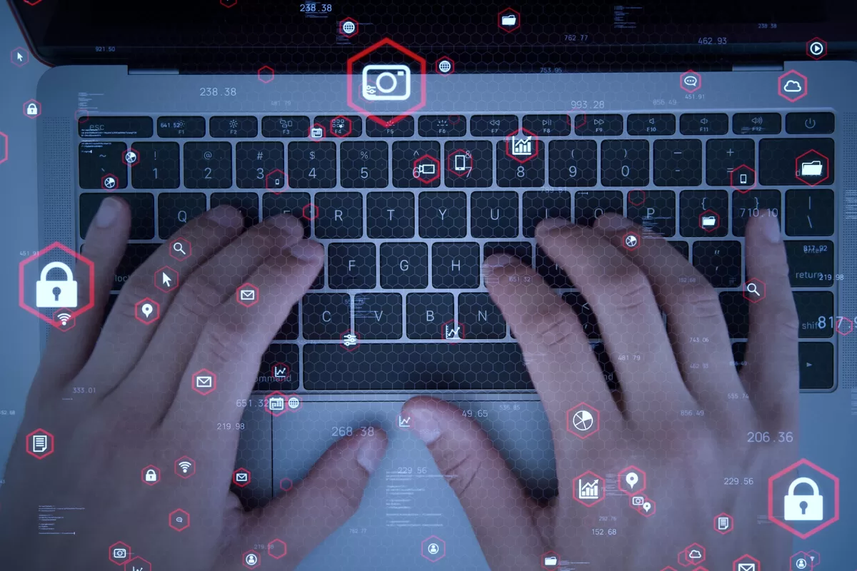 Mãos digitando em teclado de laptop com overlay de ícones digitais representando testes de segurança e automação de software, ilustrando o conceito de testes funcionais automatizados