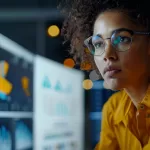 Tech professional reviewing dashboards and metric charts on multiple monitors, focused on data and performance.