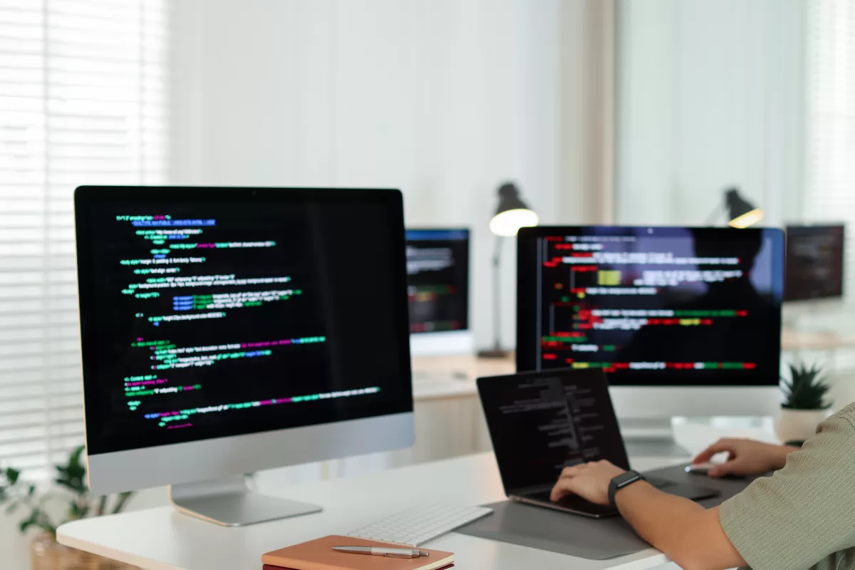 Multiple monitors displaying colorful code in development environment with developer working, representing continuous testing and production monitoring
